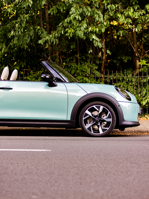 Cropped in shot of the front of a MINI Cooper Convertible in Ocean Wave Green - roof down in a neutral city location.