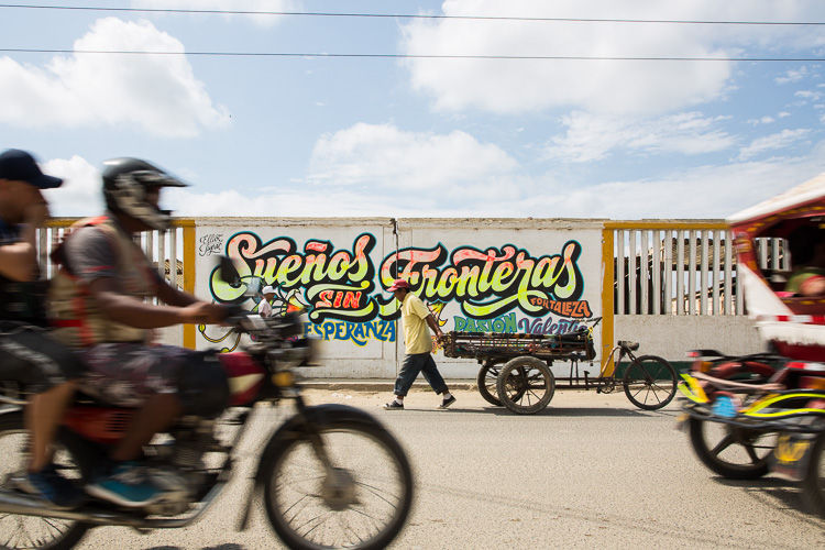 Traffic passes in front of a mural at the Ecuador-Peru border. The mural, painted by Venezuelan migrants refugees, reads "Dreams Without Borders" in Spanish.