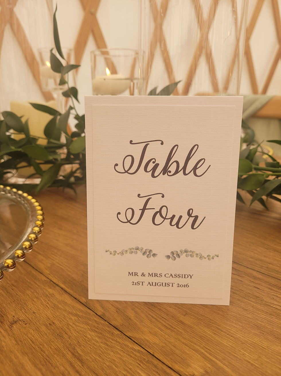 Thumbnail: This image shows the Eucalytpus Design Table Number on a rustic table set with greenery and candles.