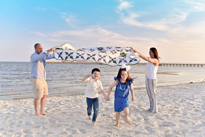 Two kids running under a blanket the parents hold while on the beach in Long Beach, MS.