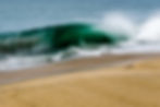 Fotografia de onda verde quebrando próxima à praia de areia.