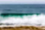 Fotografia de onda quebrando com espuma branca sobre o mar azul.
