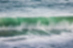 Fotografia de onda verde quebrando próximo à praia.