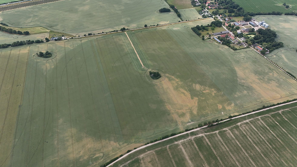 Luftaufnahme von großen Ackerflächen mit unregelmäßigen Wachstumszonen aufgrund von Trockenheit nahe einer Hofstelle.