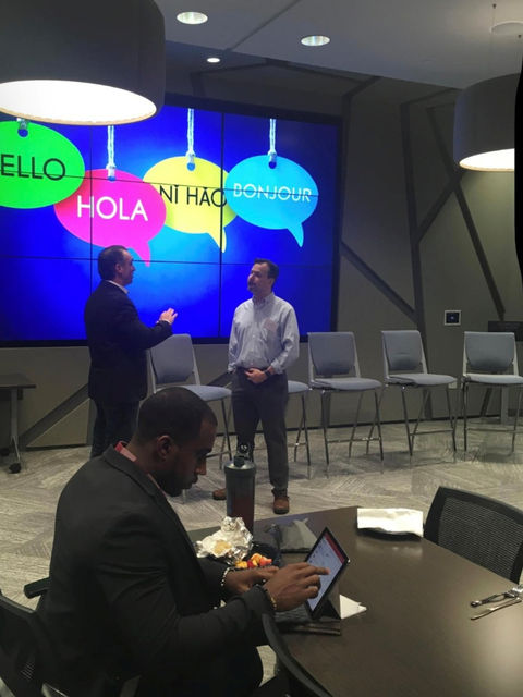 Two men in front of a screen with multiple languages, Hello, Hola, Ni Hao.