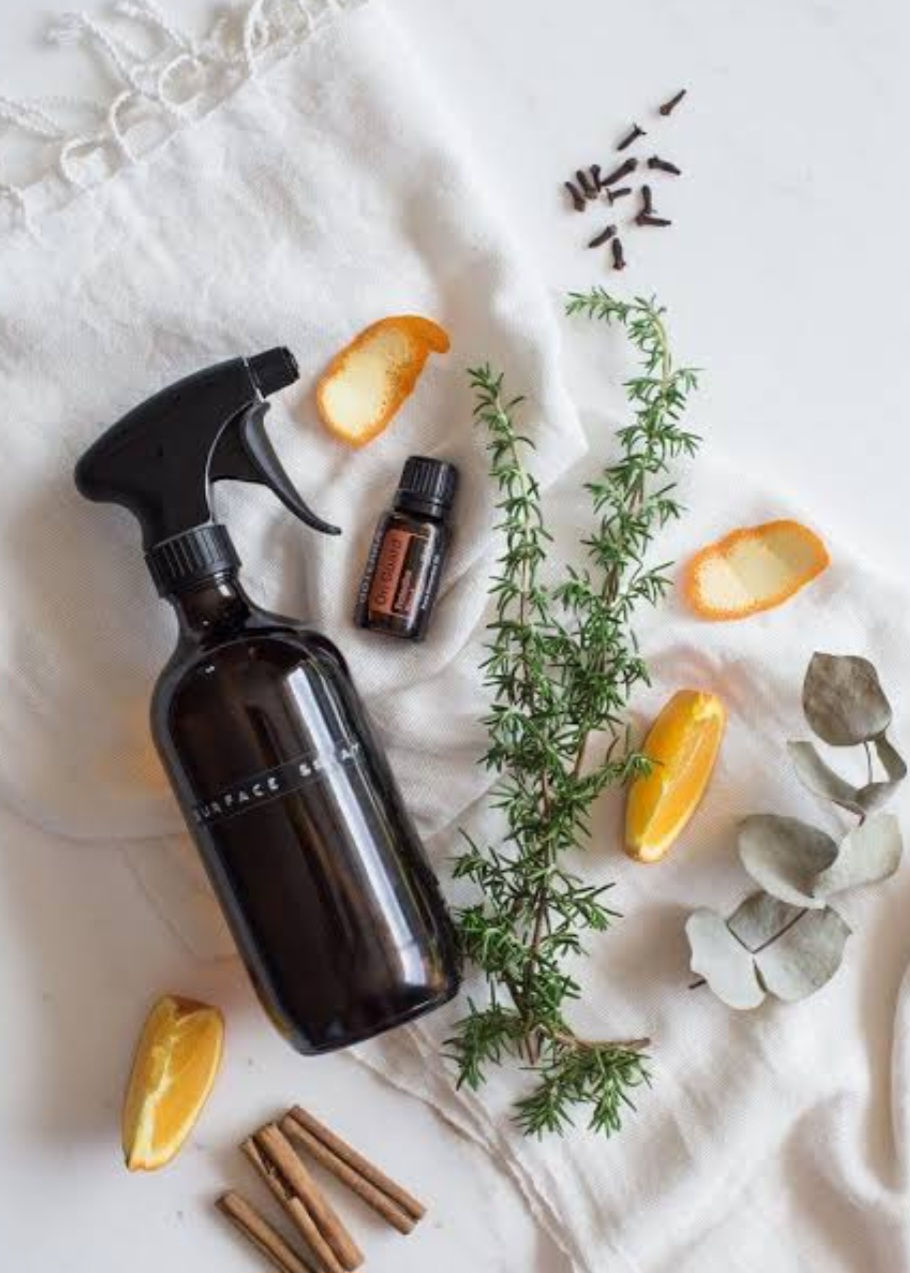 A reusable glass spray bottle full of DIY multipurpose cleaner on a table cloth surrounded by natural ingredients
