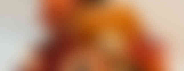 A small orange faux pumpkin with three smaller pumpkins, cream colored berries and autumn colored leaves at the base.