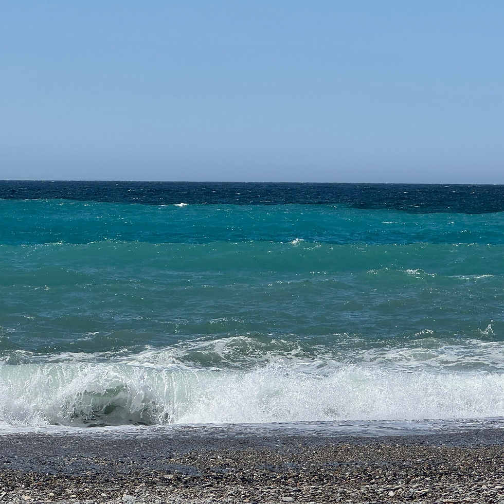 Turquoise ocean waves crash onto a pebbled beach under a clear blue sky.