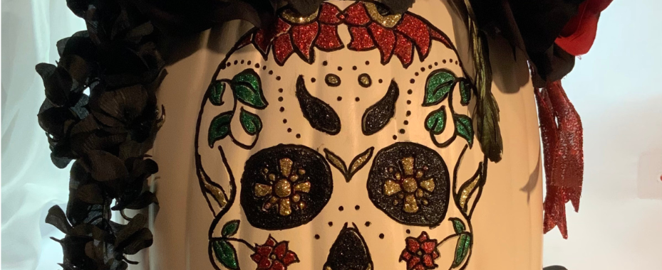 an oblong faux white pumpkin decorated with feathers, black and red flowers and a sugar skull design.