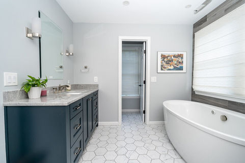 A nice modern bathroom with a soaker tub, navy cabinets, and nice quartz counters.