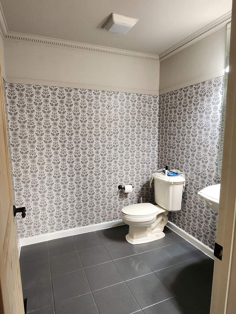 Black tile flooring, wallpaper and beige paint installed in bathroom