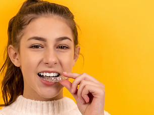 A beautiful girl puts a dental retainer on her teeth, she stands on a yellow background. O