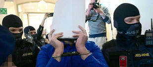 Beran A. was led into court in Wiener Neustadt escorted by masked security officials (Photo credit: Roland Schlager/APA/AFP) via BBC