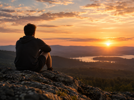 A man sits on a rocky overlook at sunset, looking across distant mountains and water, reflecting the themes of uncertainty, trust, faith, and remaining present when the future is unknown.