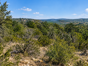 Raw undeveloped Texas Hill Country acreage with dense cedar, rocky limestone terrain, and uneven grade before land clearing and site prep work.