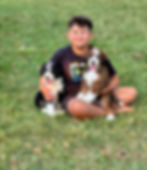 Child holding Bernedoodle puppies in a grassy yard at a North Carolina breeder focused on family-raised, well-socialized doodle puppies