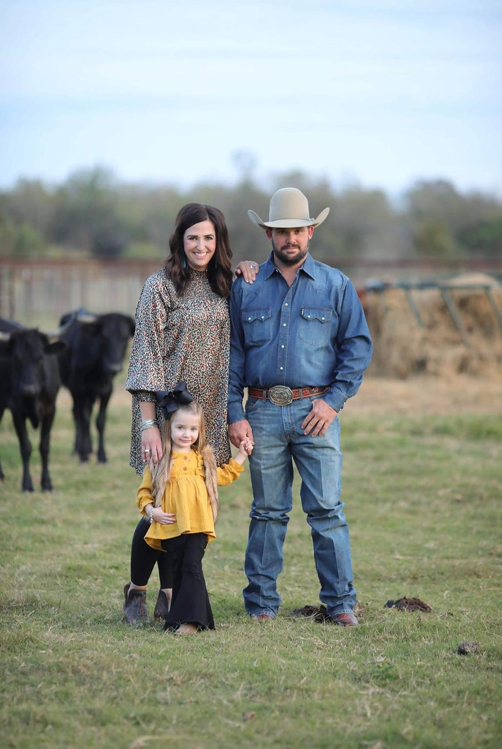 texas family of wife husband and toddler daughter in country boots with cattle and cows on a ranch