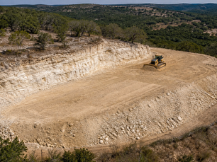 Cut-and-fill grading on a sloped Texas Hill Country lot, with exposed limestone on the uphill side and a compacted level pad below.
