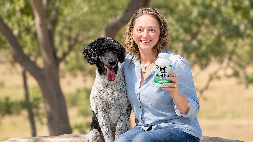 Woman holding a bottle of NuVet Plus canine wafers while sitting outdoors beside her black and white Standard Poodle in the Texas Hill Country, promoting daily dog immune support and nutritional supplementation.