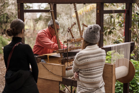 A crowd watches a man operate an old loom
