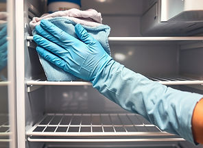 a close up of someone wiping the shelves of a fridge with gloves on.jpg