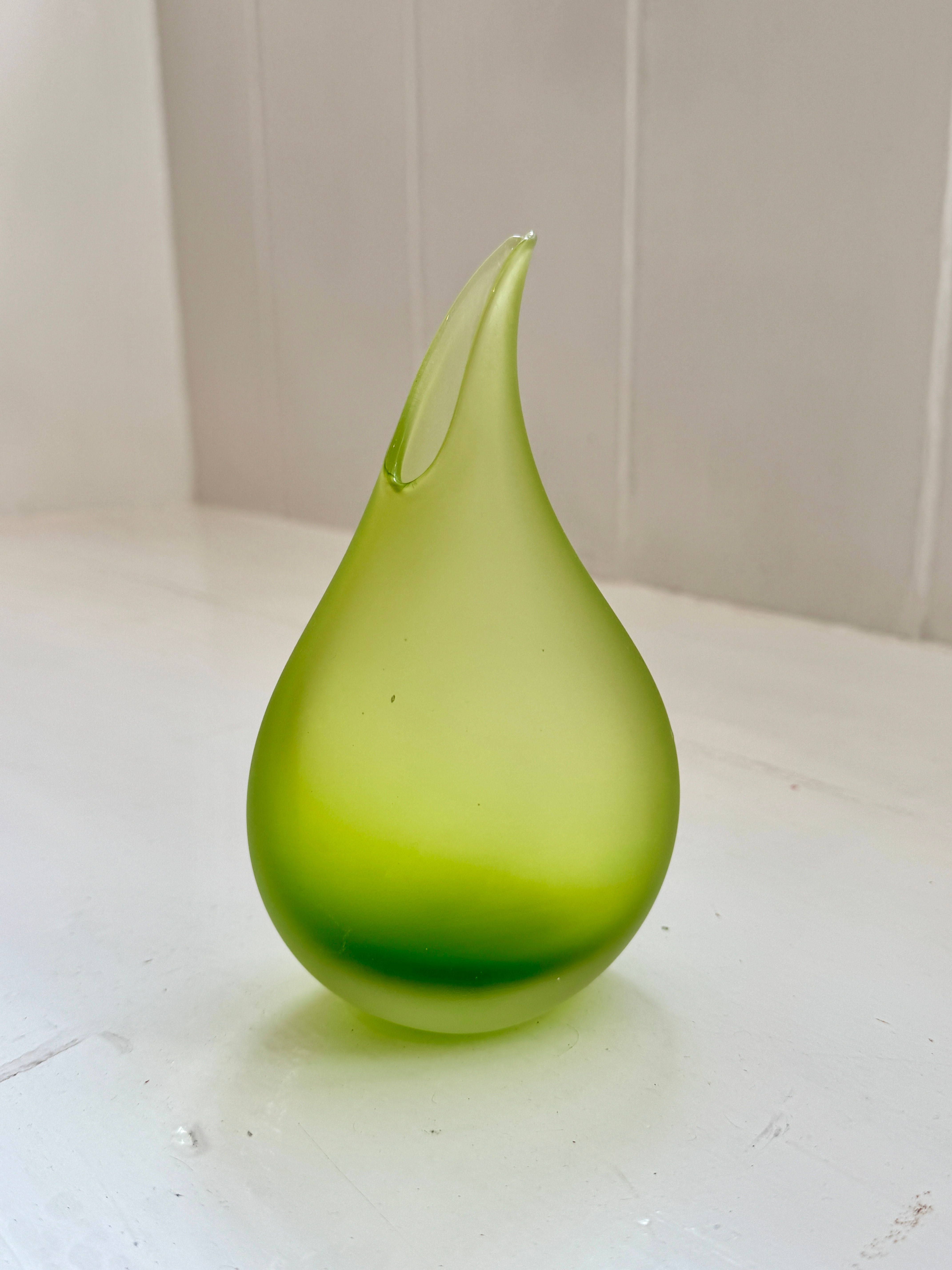 Glass vase in the shape of a tear drop in lime green colour on white shelf