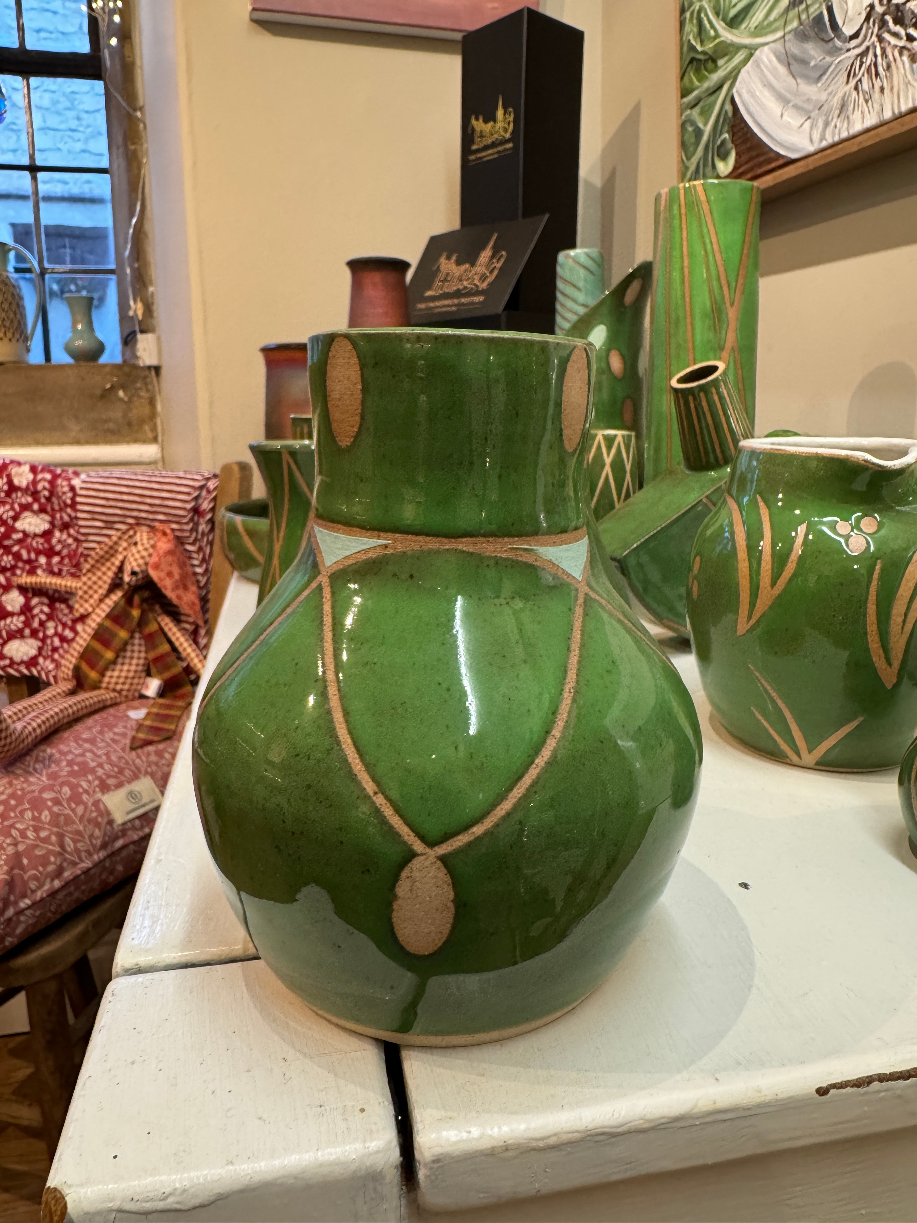 Green vase with art deco style pattern on it. Narrower at the top than the bottom half which is rounded and much wider