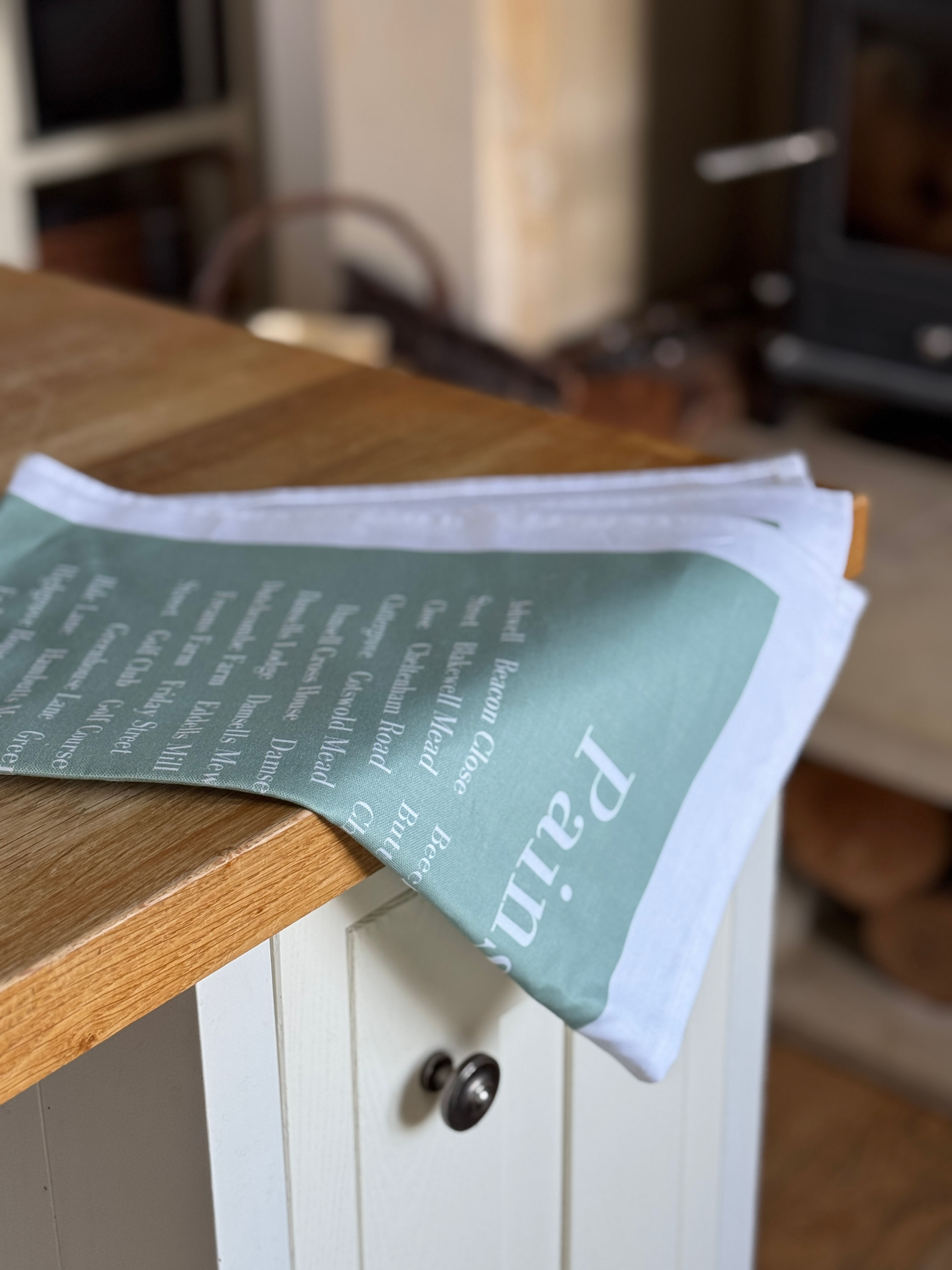Soft green tea towel with the word Painswick at the top in white and all the street name of Painswick on counter