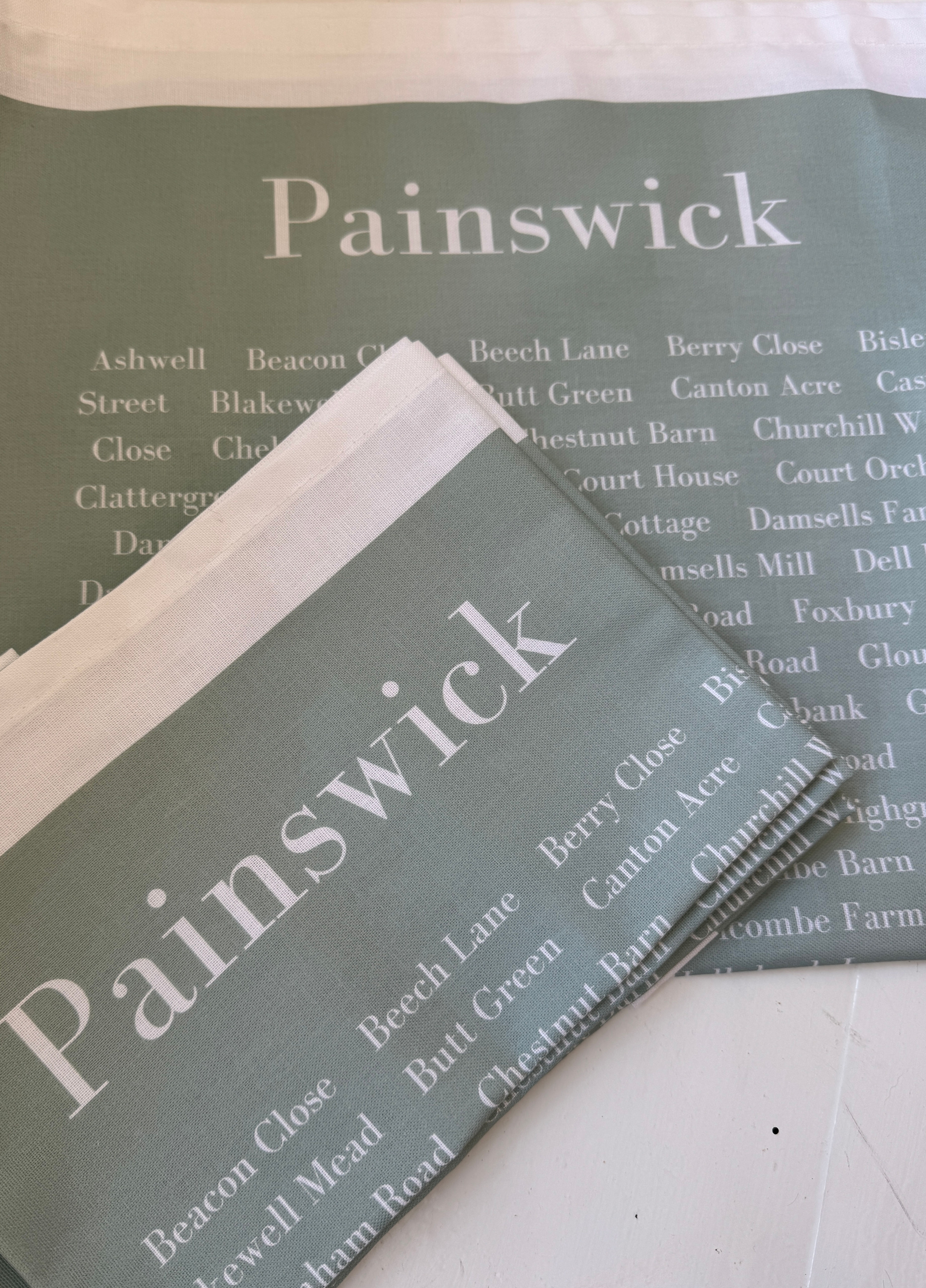 Soft green tea towel with the word Painswick at the top in white and all the street name of Painswick