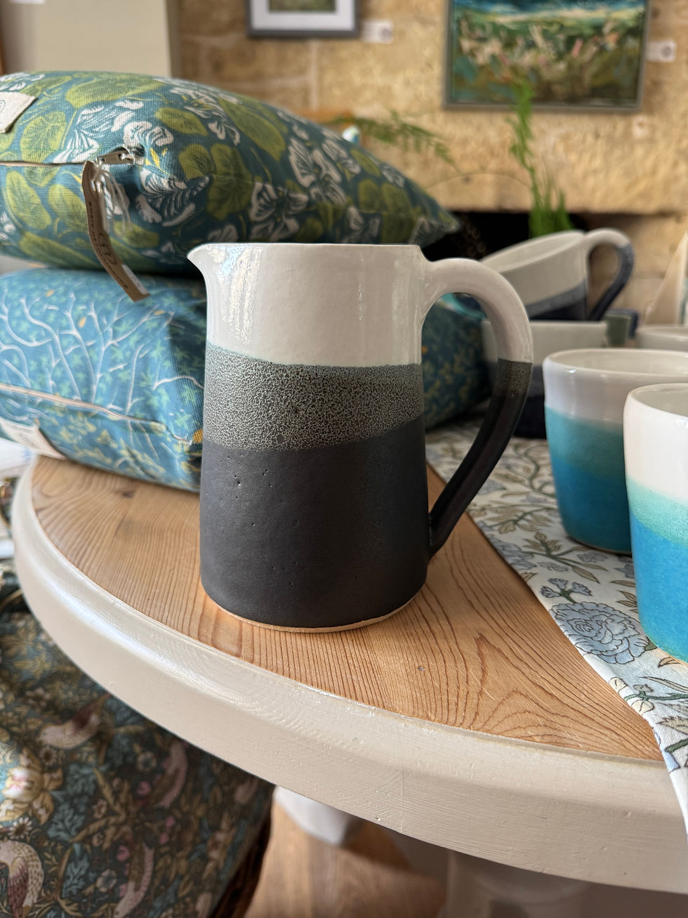 Thumbnail: Jug with black grey and cream colours on wooden top with cushions behind