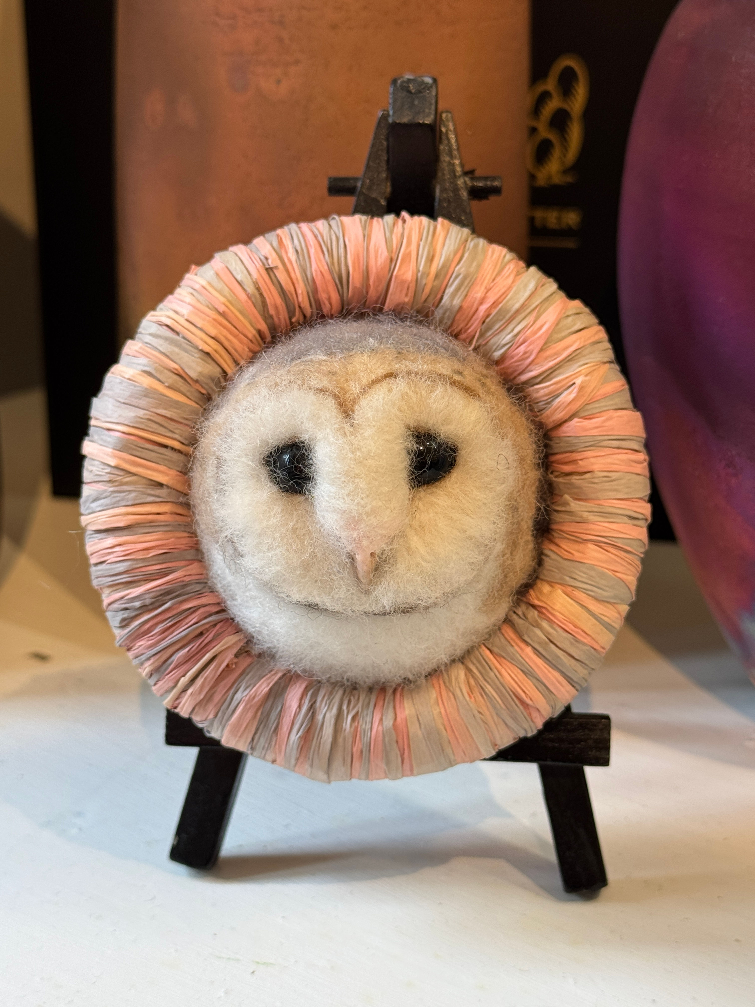 owl head in circle of pale pink on a black stand