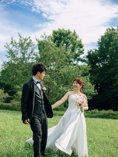 koil filmの前撮り写真 — 緑の芝生を手をつないで歩く新郎新婦の全身スナップ