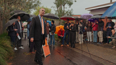Licensed auctioneer conducting a property auction for Irving G Property, with a crowd of buyers and agents gathered under umbrellas on a rainy Sydney day.