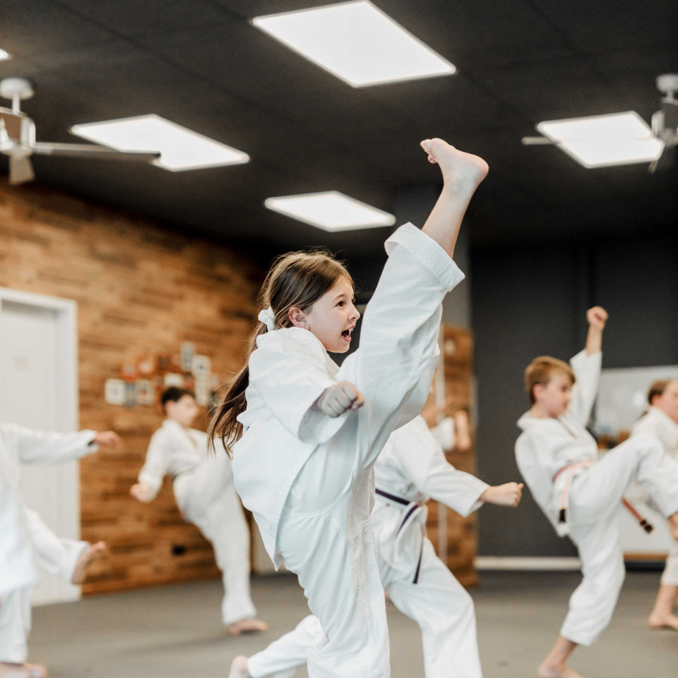Mehrere Kinder und Jugendliche üben gleichzeitig Fußtritte in der Halle.