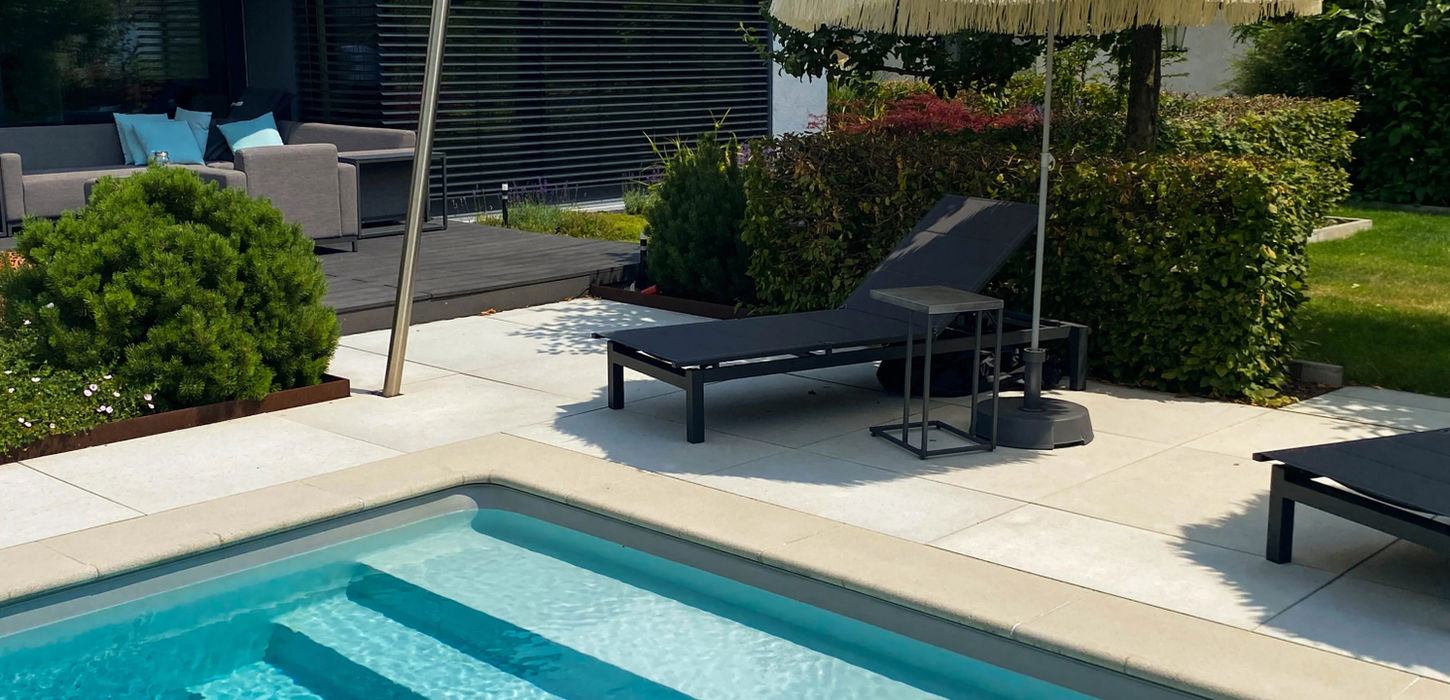 Sonnenliegen am Pool mit exotischem Sonnenschirm und schöner Bepflanzung im Hintergrund