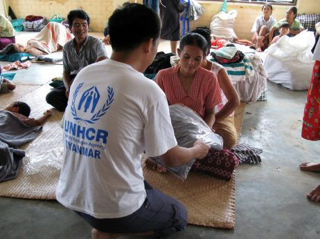 A UNHCR worker hands a blanket to a young child in Myanmar