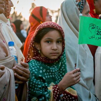 Young Pakistani girl at a women's rights demonstration holding a protest flag