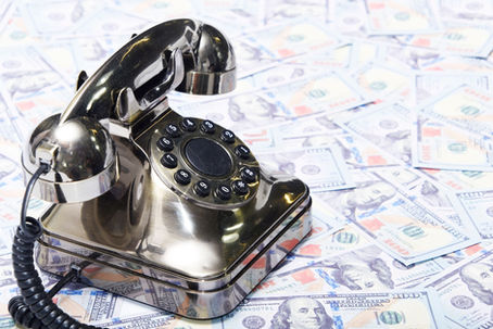 Old-fashioned telephone sitting atop a pile of money