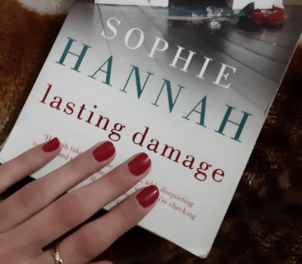 A picture of the book cover cropped so that just the title and author name is visible being held down by my red-painted fingers.