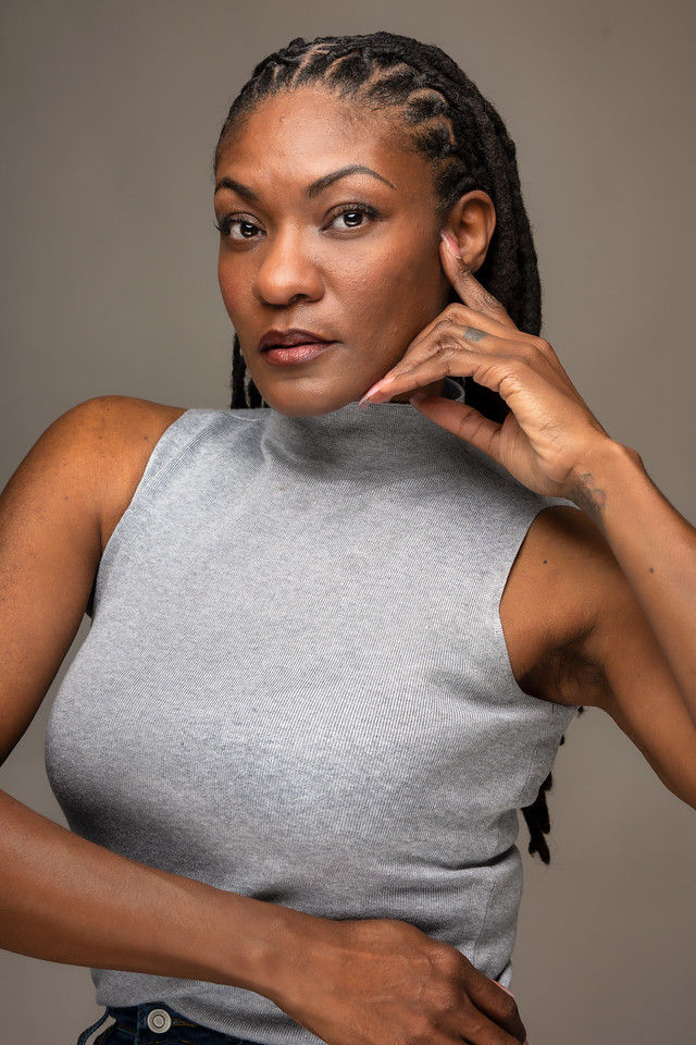 Woman with braided hair, gray top, making a 'call me' gesture.