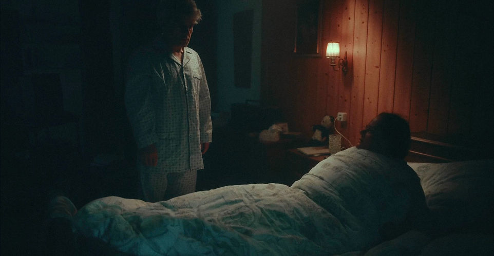 Film Still aus "Psychobilly Fever Dream"- Der Mann kommt ans Bett um der Frau schlechte Nachrichten mitzuteilen.