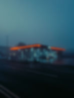 Nighttime photograph of a gas station with glowing canopy lights on a dark rural road