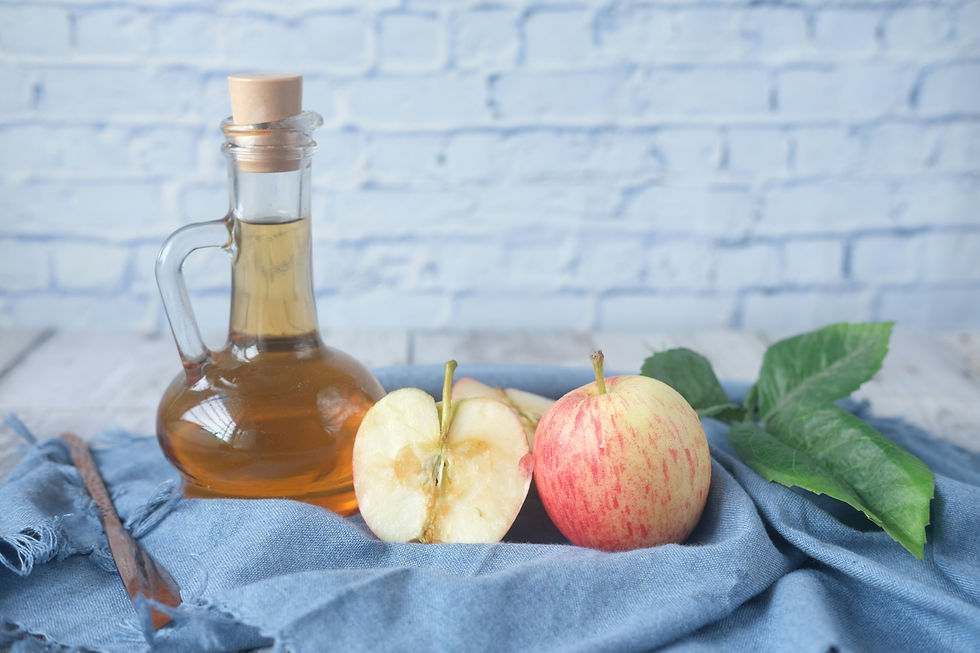 Glass jug of apple cider vinegar beside a whole and halved apple on a blue cloth, with a rustic brick background. Natural and fresh mood.