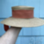 Hand holding a vintage straw hat with orange ribbon band, that has been re-blocked into shape