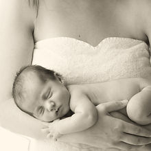 A close up of a newborn baby in a feminine presening person's arms. Close up of chest, no adult face. 