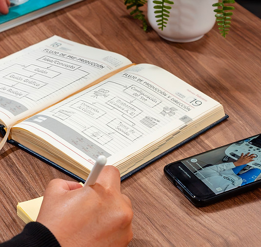 Persona escribiendo en agenda junto a smartphone en escritorio