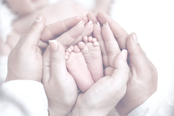 A baby is being held by a couple, with their hands around the baby's feet_edited.png