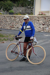 un homme en tenue d'ancien coureur montre son vieux vélo