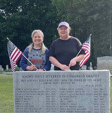 Two women holding U.S. Flags behind a stone memorial.