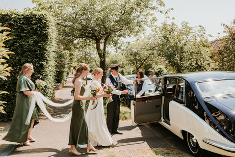 A bride and her bridesmaids entering her wedding car on a sunny day.